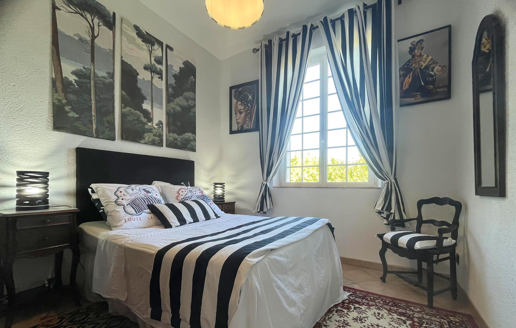 Une chambre à coucher avec un lit, une chaise, une table de chevet et une fenêtre avec des rideaux.