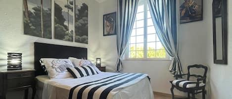 A bedroom with a bed, a chair, a nightstand, and a window with curtains.