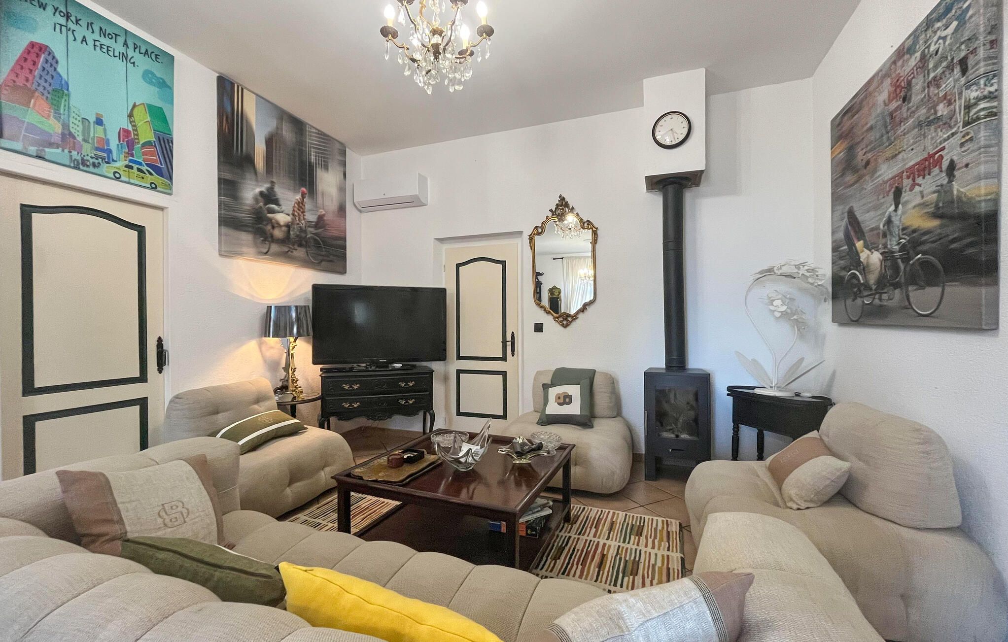 Un salon comprenant un canapé, un téléviseur, un miroir décoratif et des œuvres d’art accrochées aux murs.