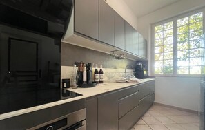 Una cocina moderna con estufa negra, gabinetes grises y ventana con vista a árboles.