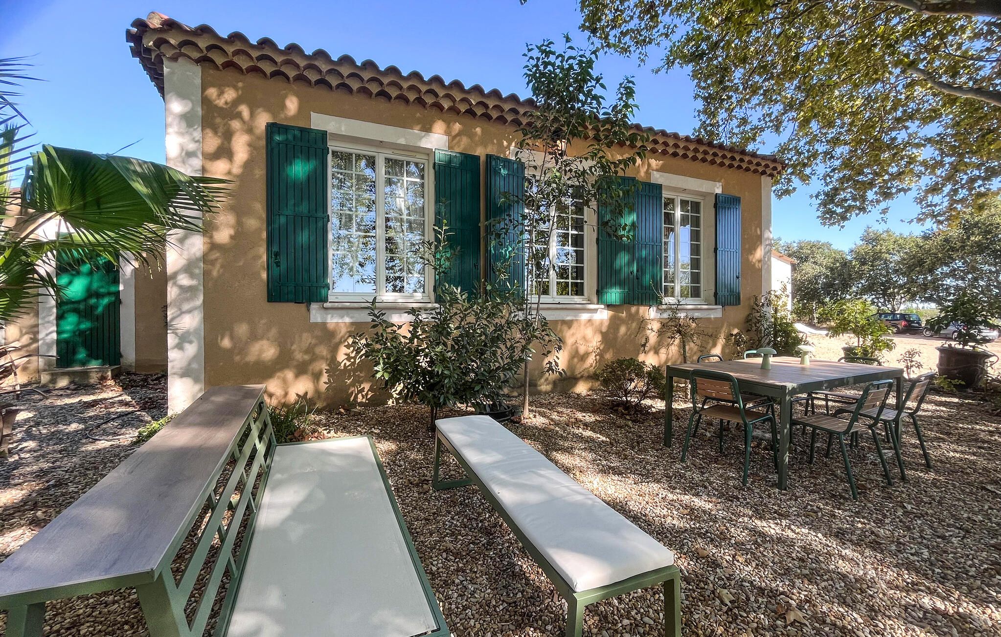 A building with a tiled roof, a patio with a table and benches, and a small garden area.