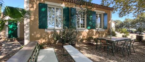 A building with a tiled roof, a patio with a table and benches, and a small garden area.