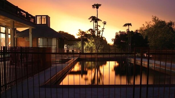 A tranquil outdoor pool area with a fence, surrounded by trees and a building with a sloped roof. - Chaminuka Luxury Lodge (Lusaka)