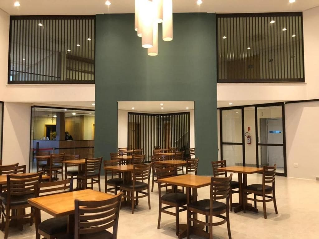 Un vaste espace dédié à la salle à manger, avec de nombreuses tables et chaises en bois, un luminaire central et une vue sur la cuisine.