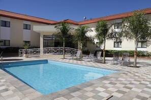Ein Pool mit Liegestühlen und Palmen, umgeben von einem Gebäude mit rotem Dach.