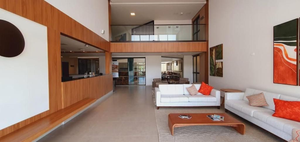 Ampla sala de estar com teto alto, sofá branco central, mesa de centro e vista para a cozinha.