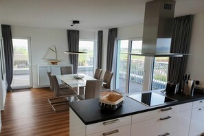 Een moderne keuken met een zwart aanrecht, witte kasten en uitzicht op het buitengebied door grote ramen.