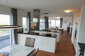 Eine moderne Küche mit einer zentralen Kochinsel, einem Essbereich mit Glastisch und Blick ins Freie.