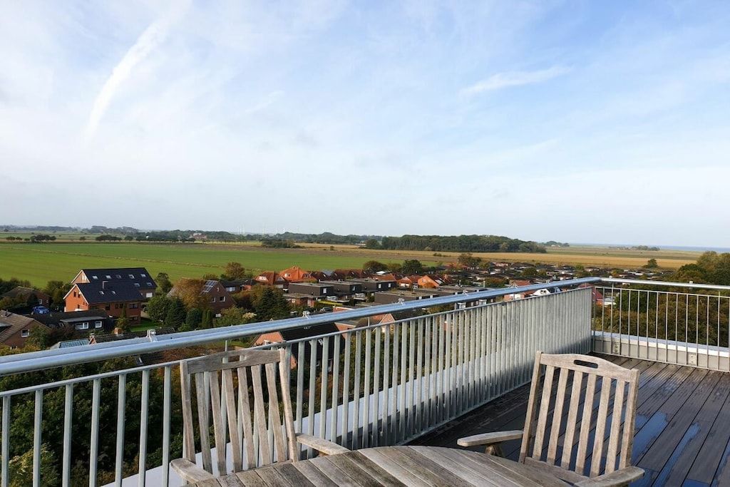 A wooden deck with a railing overlooking a residential area with houses and open fields.