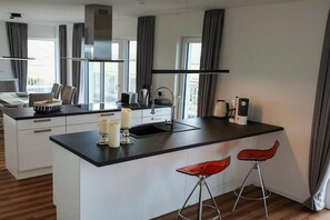 Eine moderne Küche mit einer zentralen Kochinsel, Barhocker und Blick ins Freie.