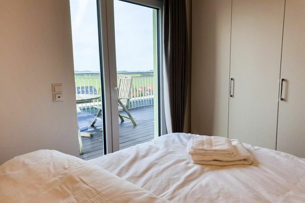 A hotel room with a bed, a window with a view of a deck, and a wardrobe.