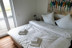 Ein Hotelzimmer mit Bett, weißen Laken, einem Bild an der Wand und einem Fenster mit Jalousien.