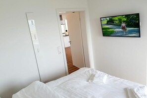 Een slaapkamer met een bed, een deur naar een badkamer en een televisie aan de muur.