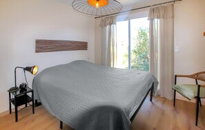 Ein Schlafzimmer mit einem Bett, einem Schreibtisch mit Lampe, einem Stuhl und einem Fenster mit Vorhängen.