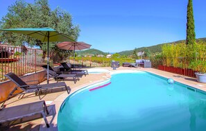Ein Pool mit Liegestühlen und Sonnenschirmen, umgeben von einem Zaun und Grünpflanzen.
