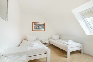 A room with two white beds, a small bedside table, a framed picture on the wall, and a sloped ceiling with a window. - "Strandperle" in Haus Rita (ID 138) (St. Peter-Ording)