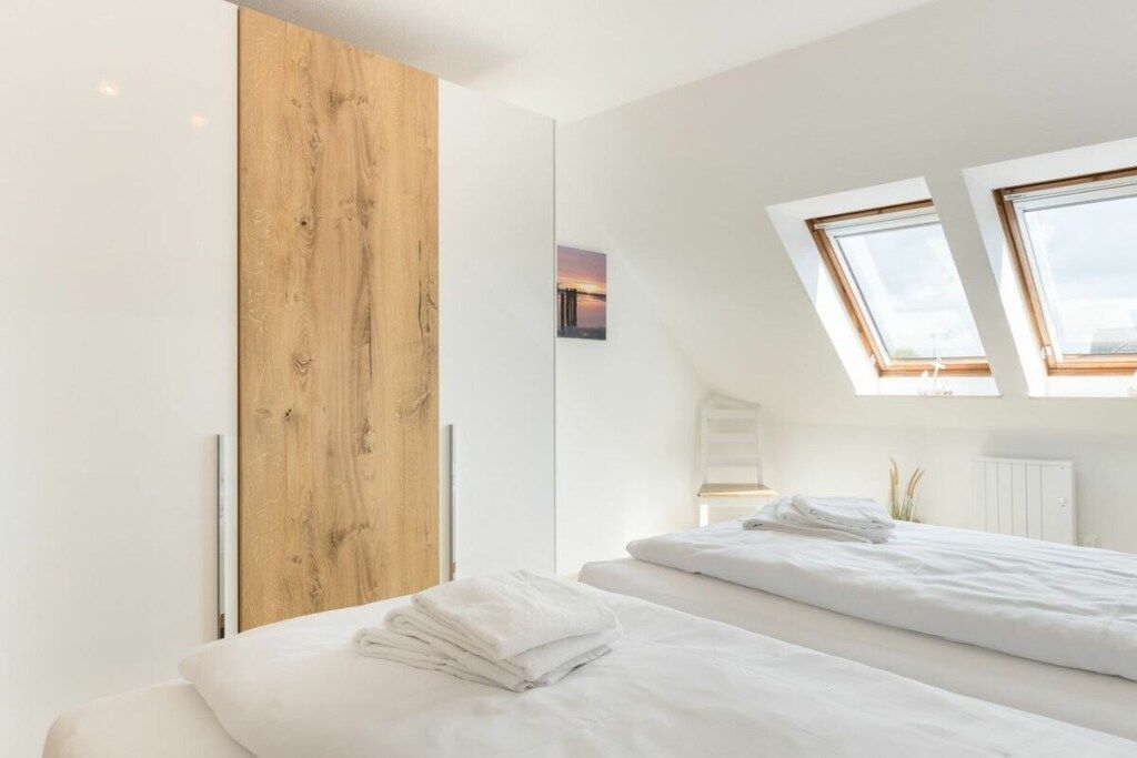 A modern bedroom with two beds, skylights, a wooden accent wall, and a small framed picture.
