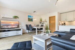 A modern living room with a flat-screen TV, a dining area, and a kitchen. - "Strandperle" in Haus Rita (ID 138) (St. Peter-Ording)