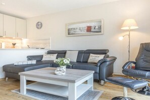 A modern living room with a grey sofa, a wooden coffee table, a black leather armchair, and a floor lamp. - "Strandperle" in Haus Rita (ID 138) (St. Peter-Ording)