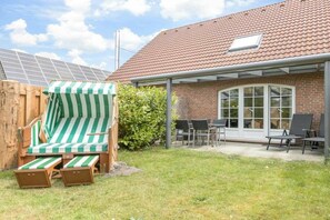 A backyard with a patio, a green-striped lounge chair, and a brick house. - "Strandperle" in Haus Rita (ID 138) (St. Peter-Ording)