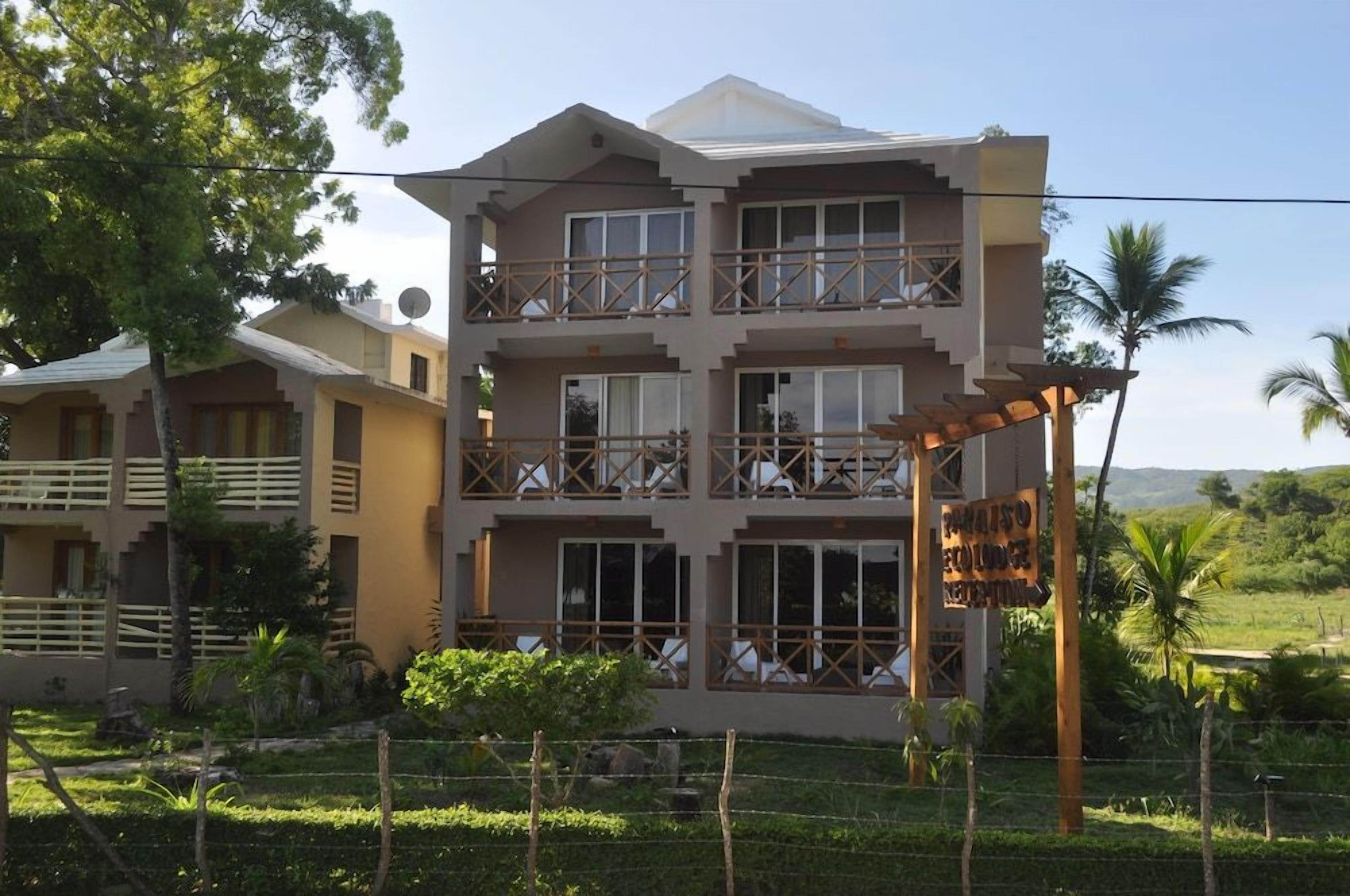 A multi-story building with balconies, surrounded by greenery and a clear sky.