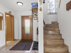 Ein Flur mit einer Holztür, einem blauen Korb auf einem Regal, einem Feuerlöscher und einer Marmortreppe.