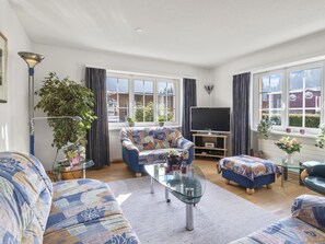 Ein modernes Wohnzimmer mit einer Couch, einem Sessel, einem Hocker und einem Glastisch.