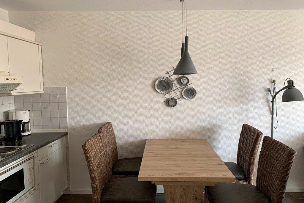 Une cuisine compacte avec un coin repas, comprenant une table en bois et des chaises en osier, un luminaire suspendu et un élément décoratif fixé au mur.