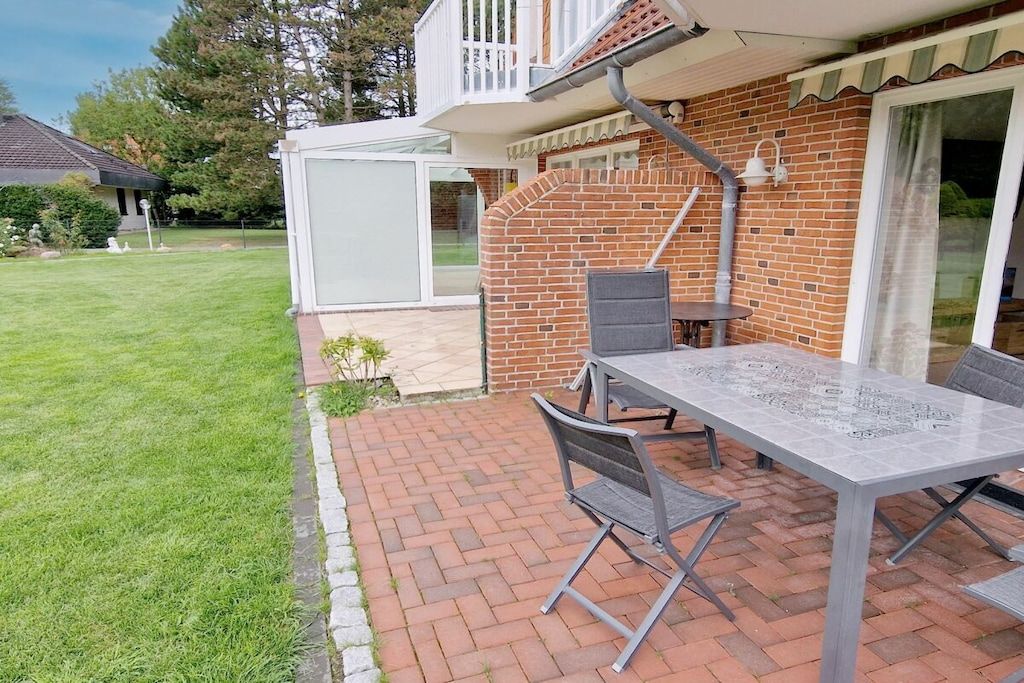 Een terras met een tafel en stoelen, een bakstenen muur en een glazen deur die leidt naar een overdekt gebied.