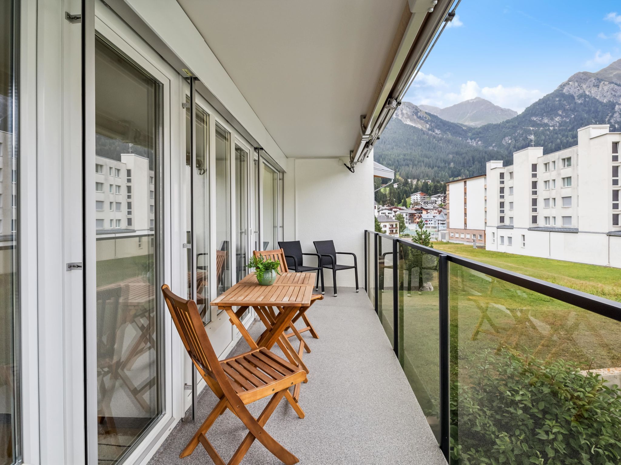 Een balkon met een houten tafel en stoelen, een bloempot en uitzicht op een bergachtig landschap.