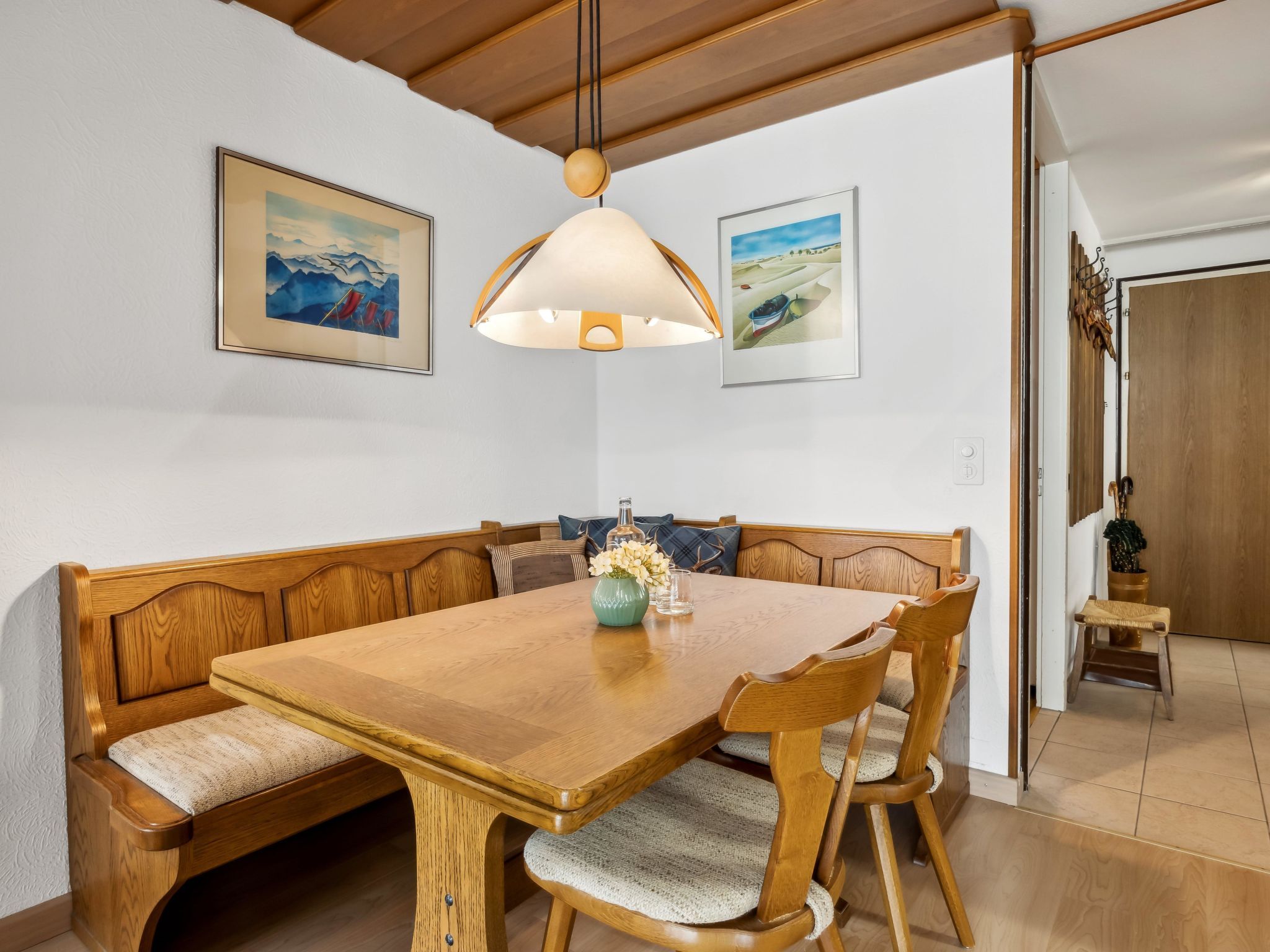 Zona pranzo con tavolo e panca in legno, una lampada a sospensione e due quadri appesi al muro.