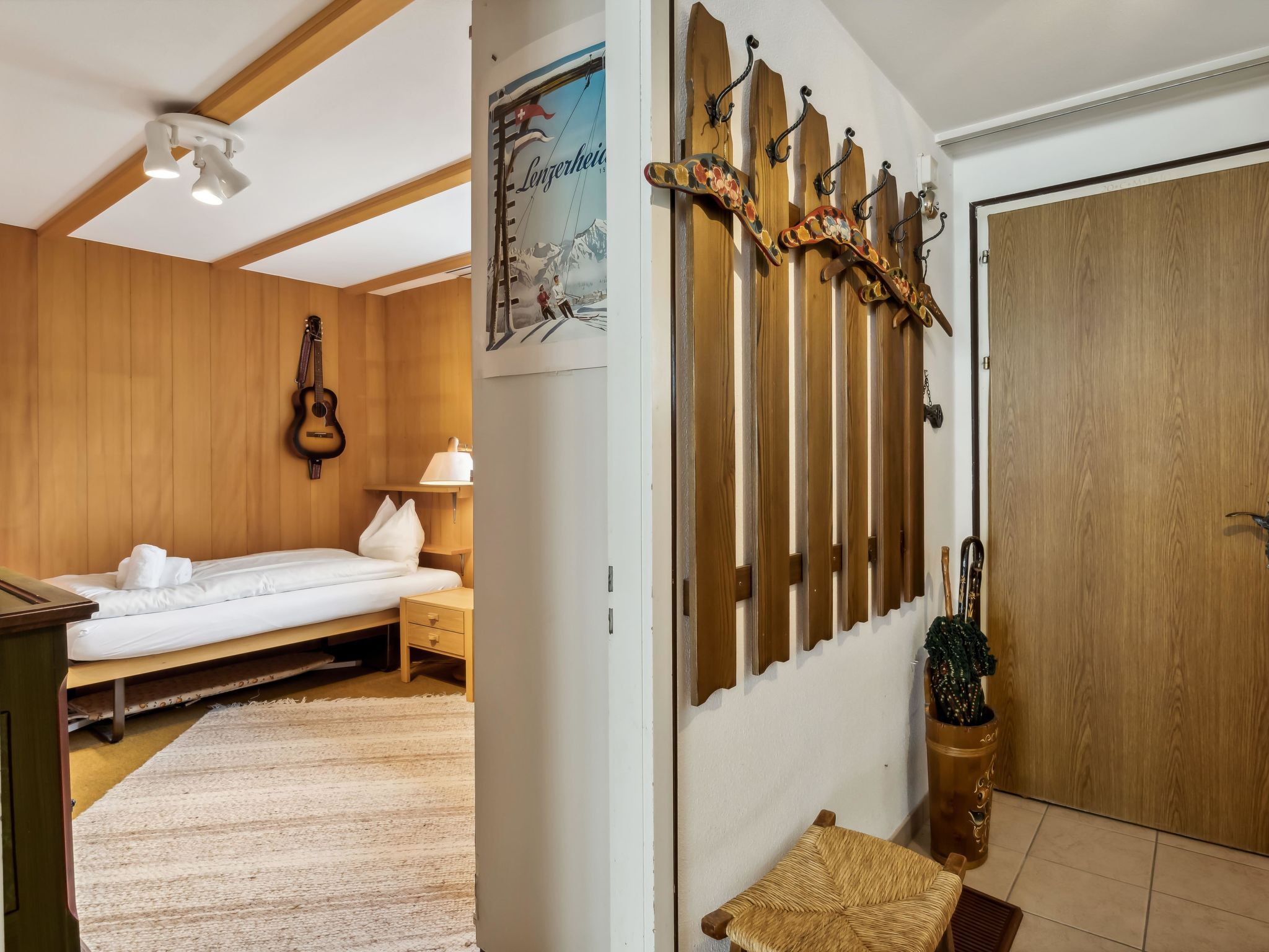 A room with a bed, a guitar, a wooden wall with hooks, a poster, and a door.