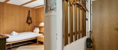 A room with a bed, a guitar, a wooden wall with hooks, a poster, and a door.