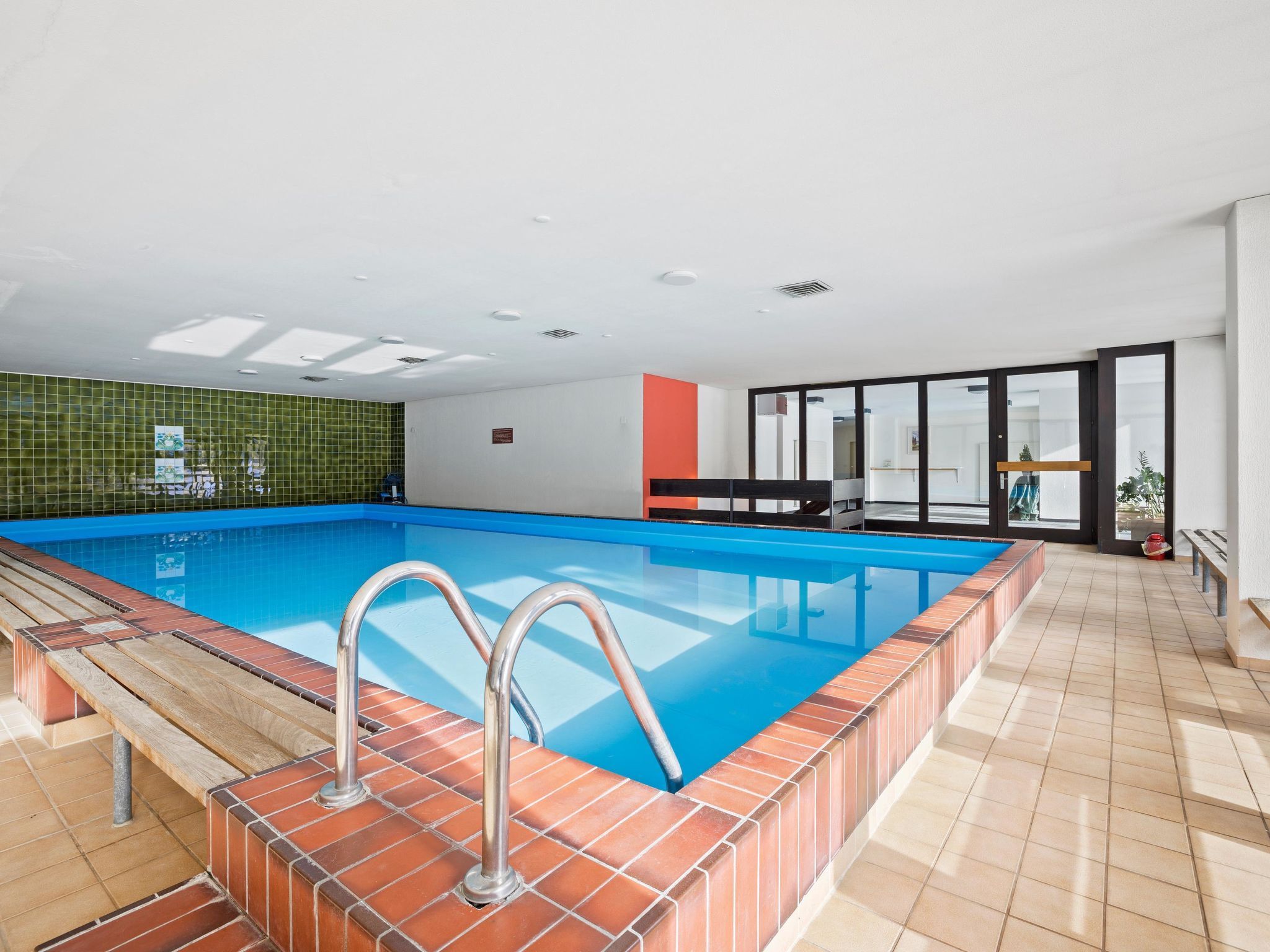 Una piscina interna con vista diretta sull'area della piscina, una parete piastrellata e una panchina.