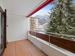 Ein Balkon mit Holzboden, Metallgeländer und Blick auf schneebedeckte Bäume und Berge.