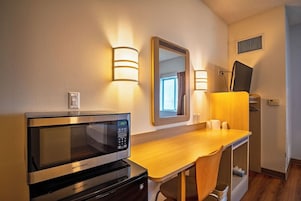 Una habitación de hotel compacta con kitchenette, un escritorio de madera, un espejo y un televisor.