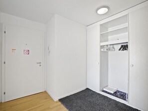 Ein Zimmer mit einer weißen Tür, einem grauen Teppich und einem weißen Kleiderschrank mit darin hängender Kleidung.