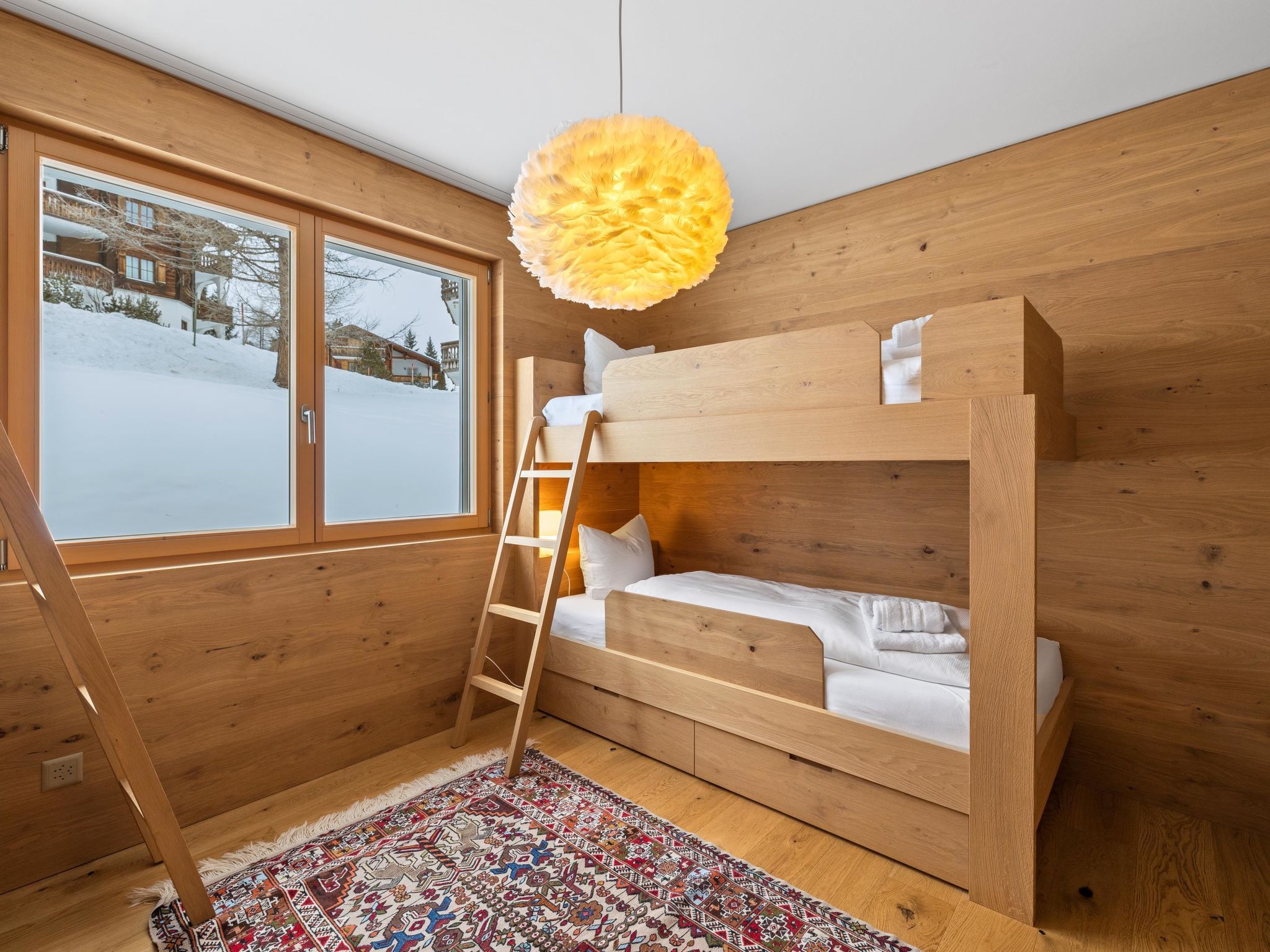 A wooden bunk bed room with a ladder, a patterned rug, and a window with a snowy view.