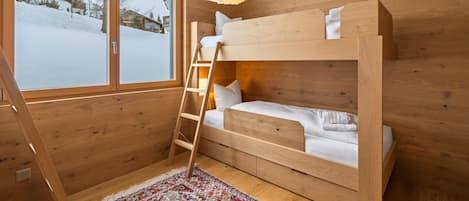 A wooden bunk bed room with a ladder, a patterned rug, and a window with a snowy view.