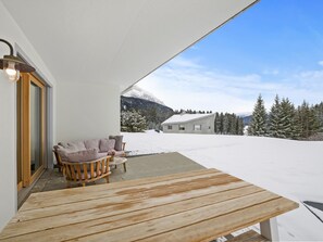 A covered outdoor seating area with a wooden table and chairs, a view of a snowy landscape with trees and mountains in the background. - Praval Appartement/Fewo Ferienwohnung Praval IH by Interhome (Valbella)
