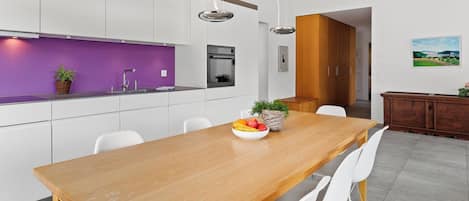 A modern kitchen with white cabinets, a purple backsplash, and a wooden dining table with chairs.