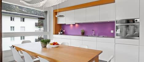 Een moderne keuken met witte kasten, een houten eettafel en een paars aanrechtpaneel.