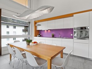 A modern kitchen with white cabinets, a wooden dining table, and a purple backsplash. - Parvenda Appartement/Fewo Ferienwohnung Parvenda IH by Interhome (Lenzerheide)