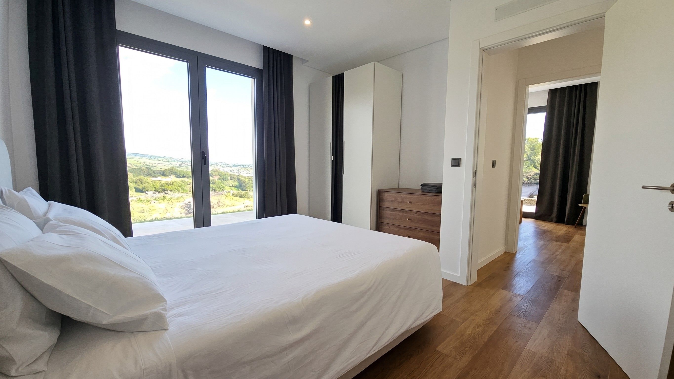A bedroom with a large bed, a wooden dresser, and a view of the outdoors through a window.