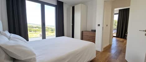 A bedroom with a large bed, a wooden dresser, and a view of the outdoors through a window.