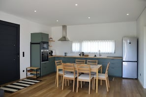 Cozinha compacta com mesa e cadeiras, forno embutido e geladeira.