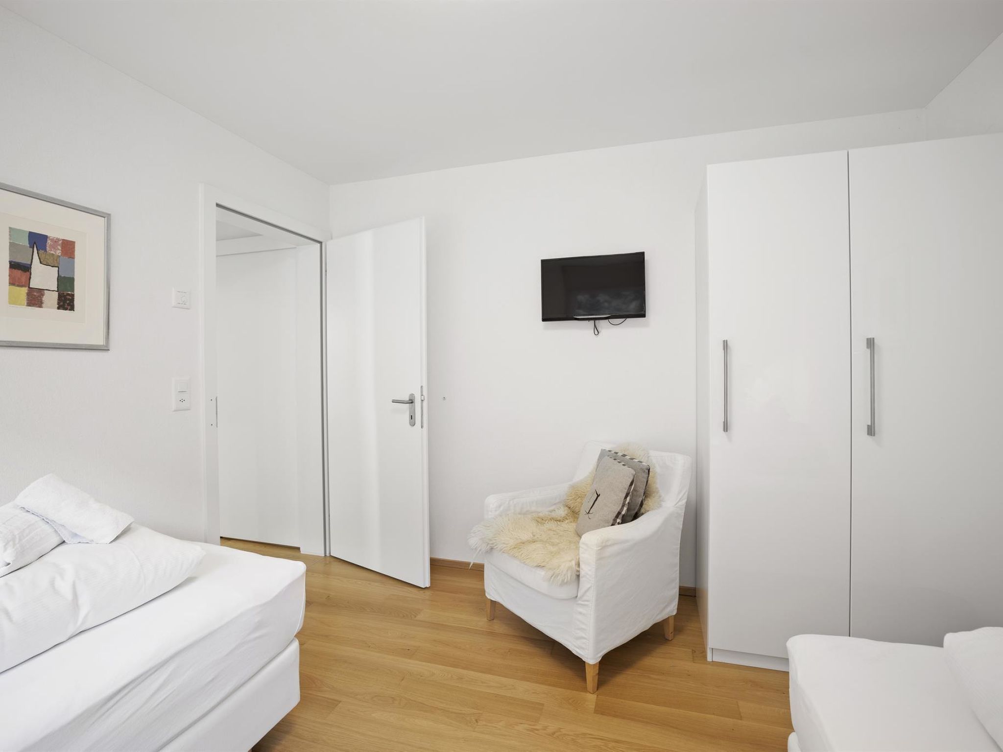 Une chambre à coucher au style minimaliste, comprenant un lit, une chaise, un téléviseur et des armoires.
