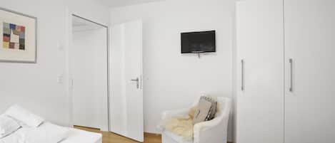 Une chambre à coucher au style minimaliste, comprenant un lit, une chaise, un téléviseur et des armoires.