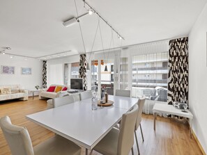 A modern living room with a white sofa, a dining table, and a kitchen area visible through a glass door. - Nr.55 Haus Sotmirana Appartement/Fewo,   Nr.55 Haus Sotmirana by Interhome (Lenzerheide)