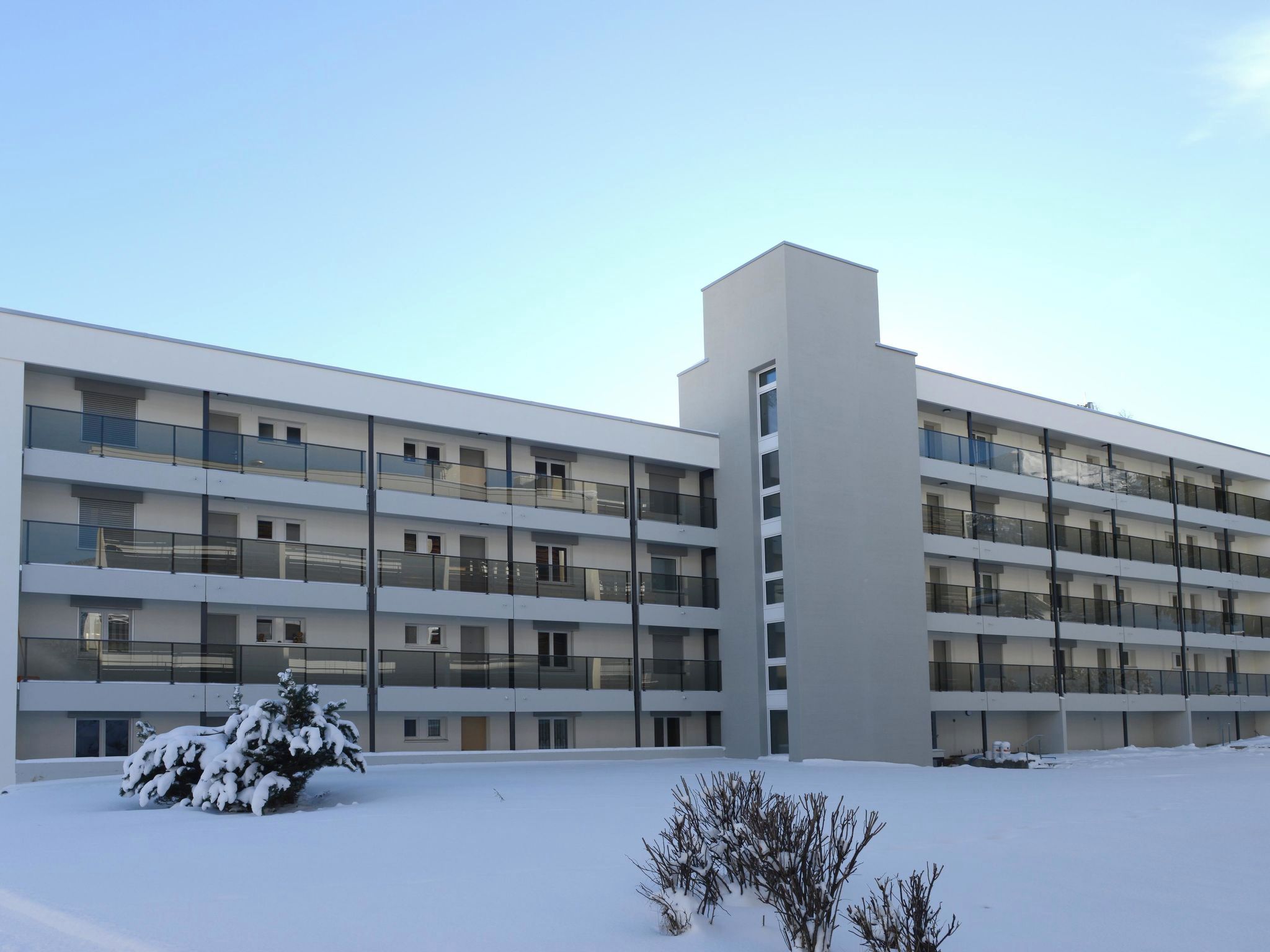 A multi-story building with balconies, a flat roof, and a snow-covered ground.